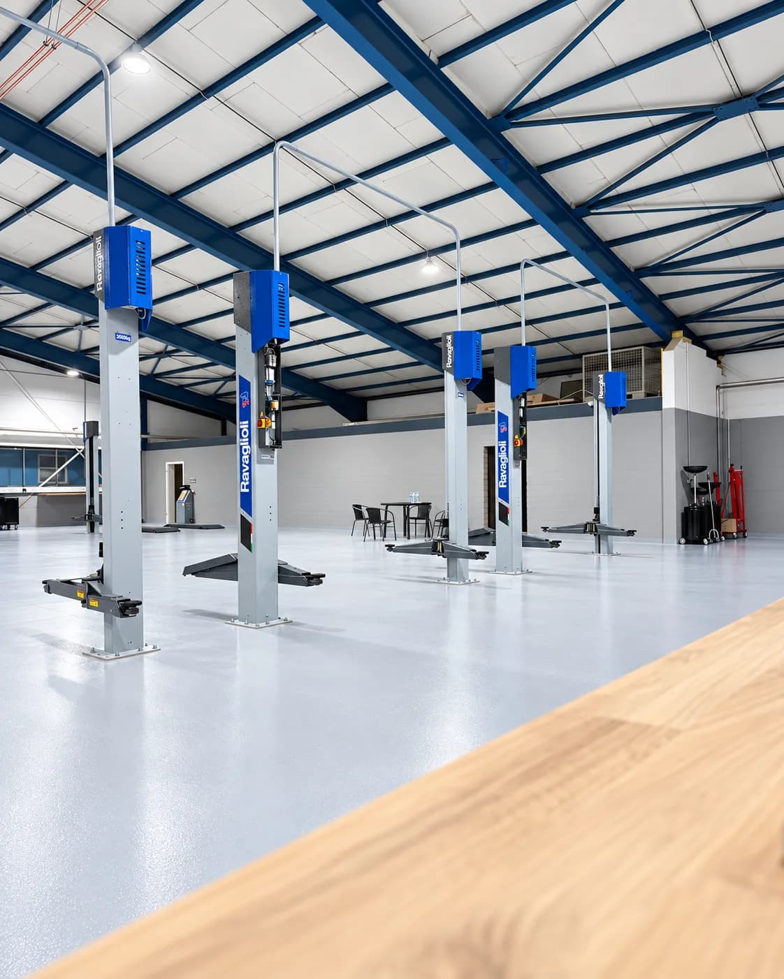 Hebebühnen und Sitzecke mit Tisch und Stühlen in der Halle, vorne eine Werkbank aus Holz