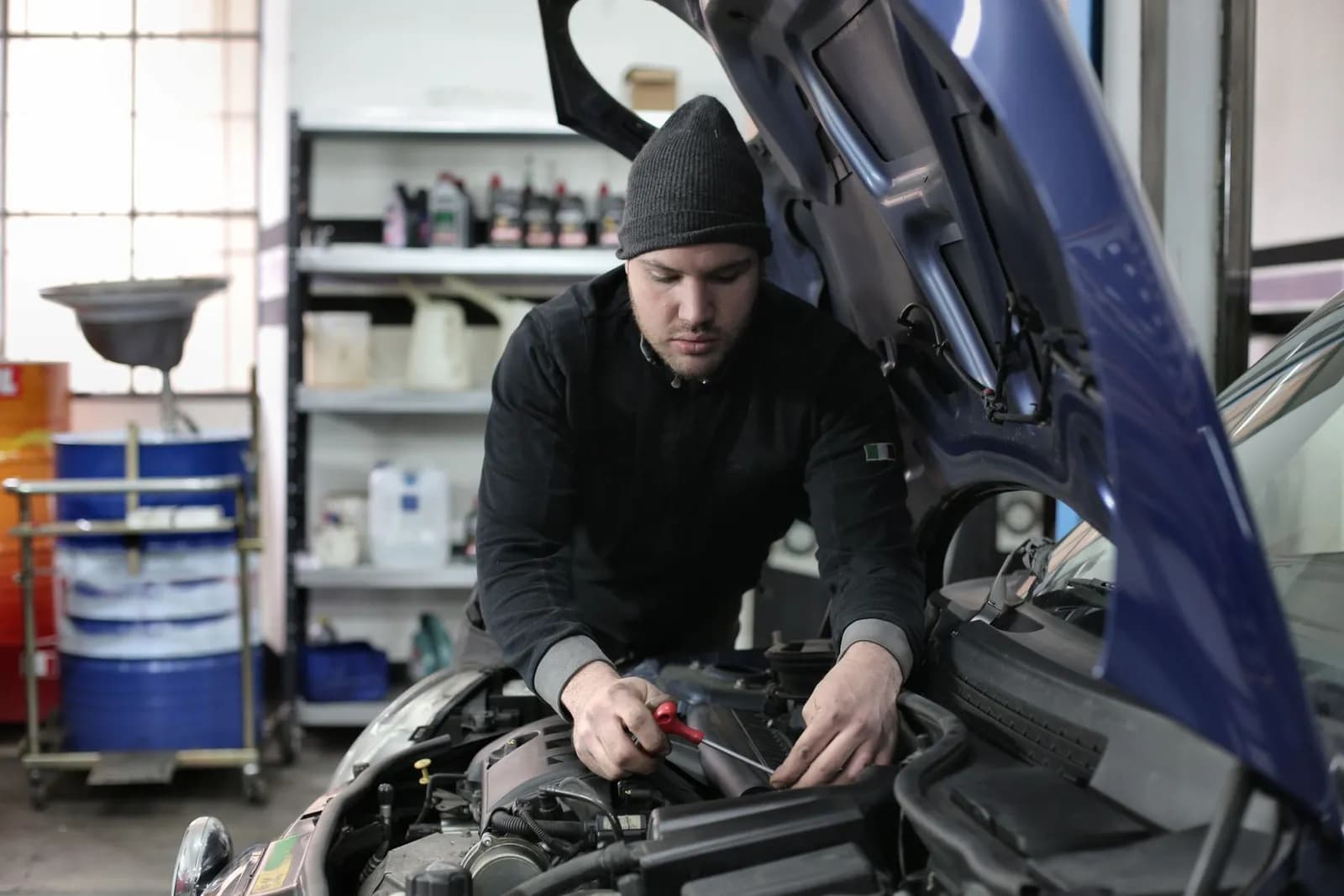 Mann mit Mütze arbeitet im Motorraum eines Autos